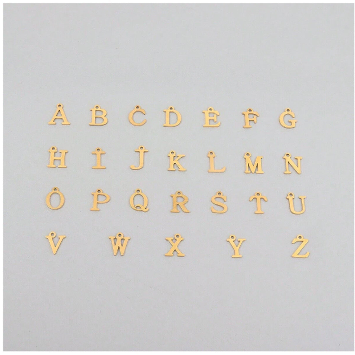 Gold alphabet letters for a necklace on a light grey background