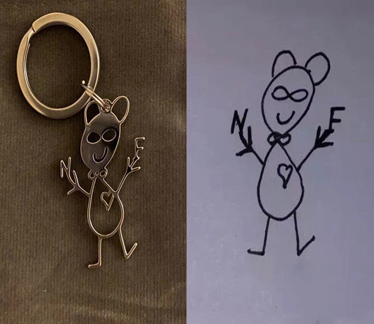 Bronze keychain with a cartoon character and a hand-drawn illustration of the same character on grey paper.