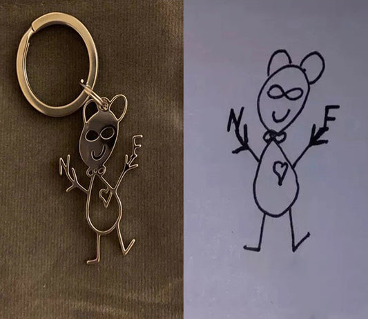 Bronze keychain with a cartoon character and a hand-drawn illustration of the same character on grey paper.