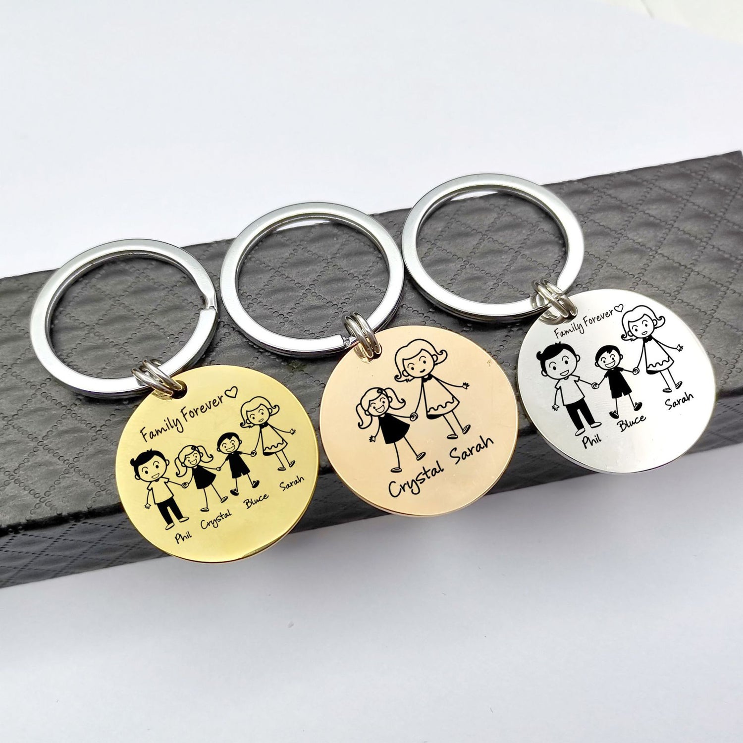 Three keychains with engraved family illustrations on a grey surface