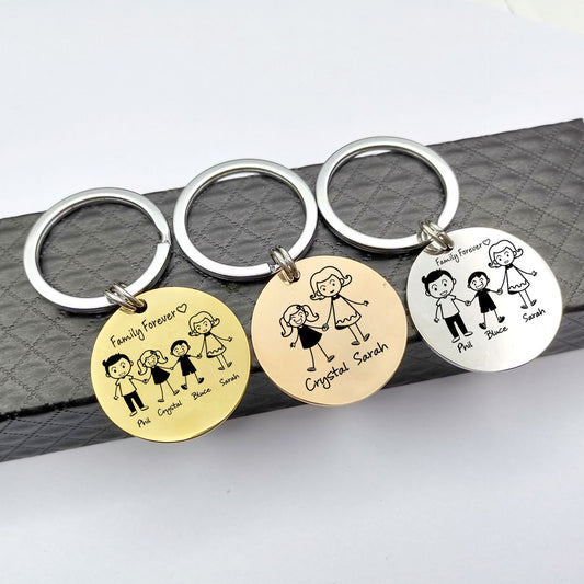 Three keychains with engraved family illustrations on a grey surface