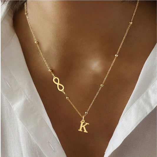 Gold necklace with infinity symbol and 'K' pendant on a person wearing a white shirt.